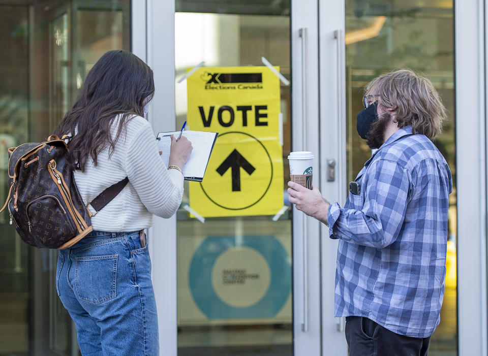 An Elections Canada worker, right, holds a voter's coffee as they record COVID-19 contact-tracking information at the Halifax Convention Centre as they prepare to vote in the federal election in Halifax on Monday, Sept. 20, 2021. (Andrew Vaughan/The Canadian Press via AP)