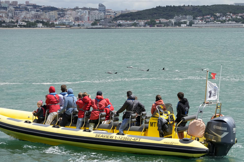 Tourists watch dolphins swim near their boat at the mouth of the Tagus River with Lisbon in the background, Friday, June 24, 2022. Starting Monday the United Nations is holding its five-day Oceans Conference in Lisbon hoping to bring fresh momentum for efforts to find an international agreement on protecting the world's oceans. (AP Photo/Armando Franca)