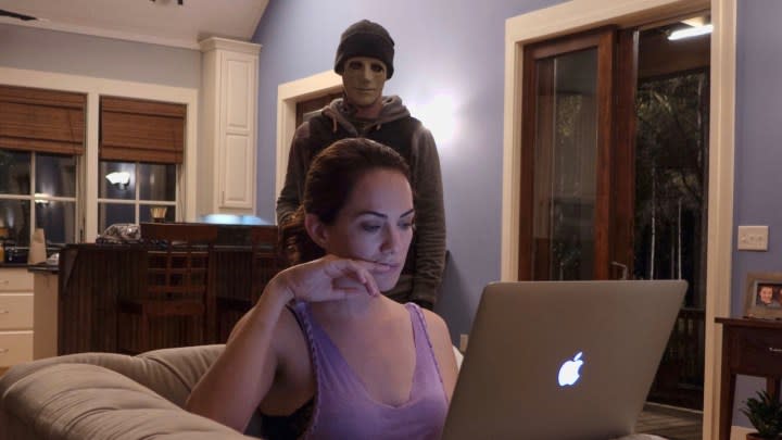 A masked killer watches Kate Siegel work in a scene from "Hush."