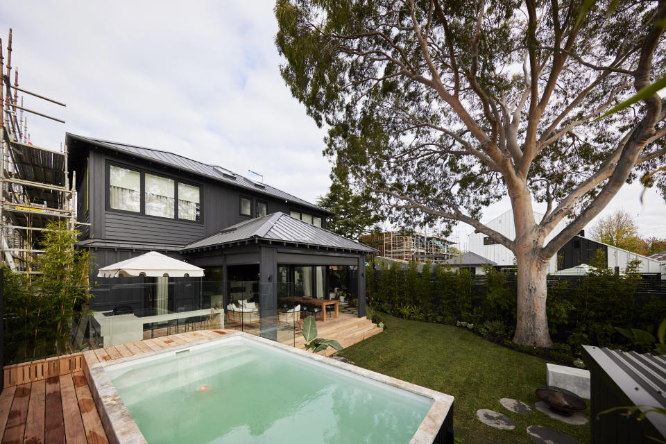 A shot of the pool, with a gazebo like area at the back of the house and a large gum tree in the back right corner. 