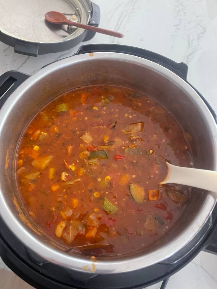 Pot of soup with vegetables cooking in an Instant Pot. A ladle rests on the side