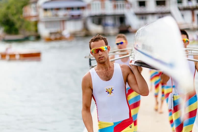 Rowers, wearing striped shorts, carrying racing shell at Henley-on-Thames, Oxfordshire, England