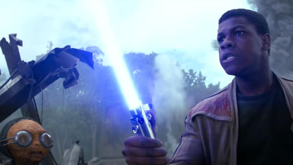 Man holding a lightsaber next to a robot, intense expression, debris and smoke in background