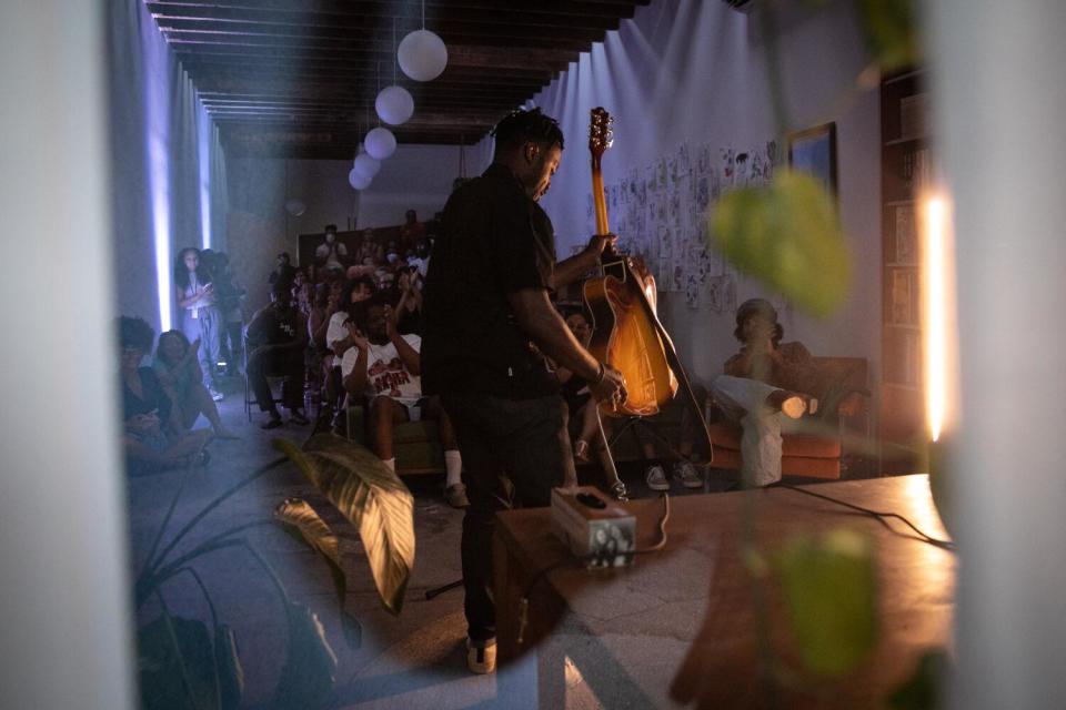 A Black man on stage holding a guitar in front of a crowd.