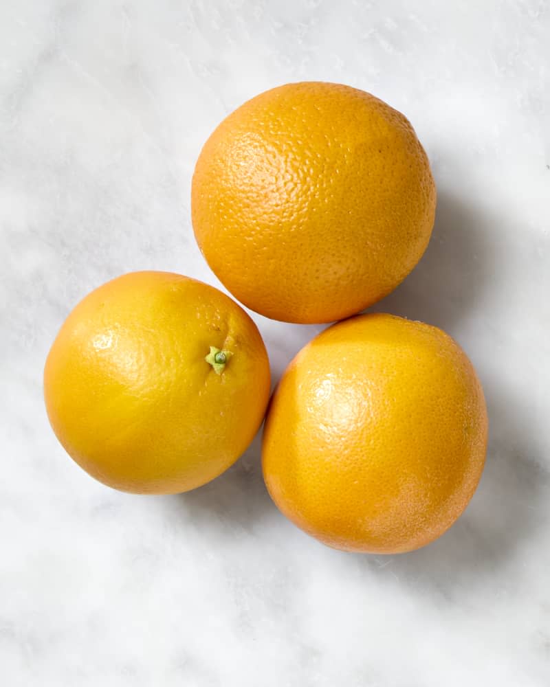 overhead shot of three valencia oranges on a marble surface.