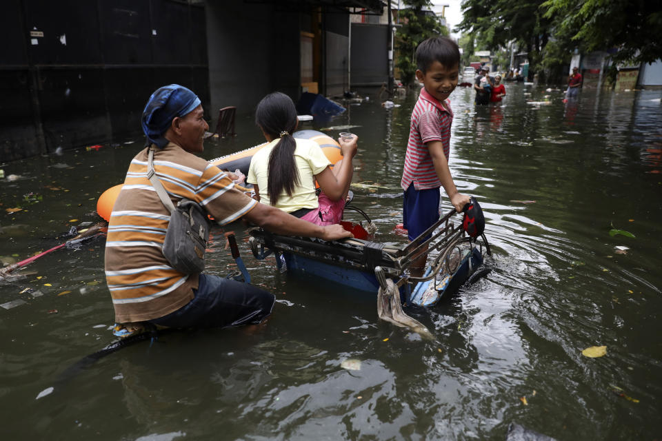 A young boy reacts as he rides on a tricycle with his father and sister at a flooded neighborhood in Jakarta, Indonesia, Saturday, Jan. 4, 2020. Monsoon rains and rising rivers submerged parts of greater Jakarta and caused landslides in Bogor and Depok districts on the city's outskirts as well as in neighboring Lebak, which buried a number of people. (AP Photo/Dita Alangkara)