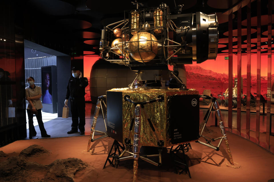 A security guard and worker stand near a depiction of a Chinese lander in a Mars-like environment in Beijing on Friday, May 14, 2021. China says its Mars probe and accompanying rover are to land on the red planet sometime between early Saturday morning and Wednesday Beijing time. (AP Photo/Ng Han Guan)