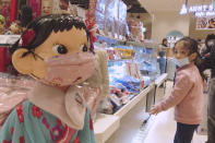 A girl wears a face mask to help curb the spread of the coronavirus and looks at a doll wearing the same at a department store in Taipei, Taiwan, Saturday, Feb. 27, 2021. (AP Photo/Chiang Ying-ying)