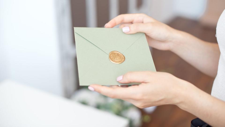 close up photo of female hands holding invitation envelope with a wax seal, a gift certificate, a postcard, wedding invitation card