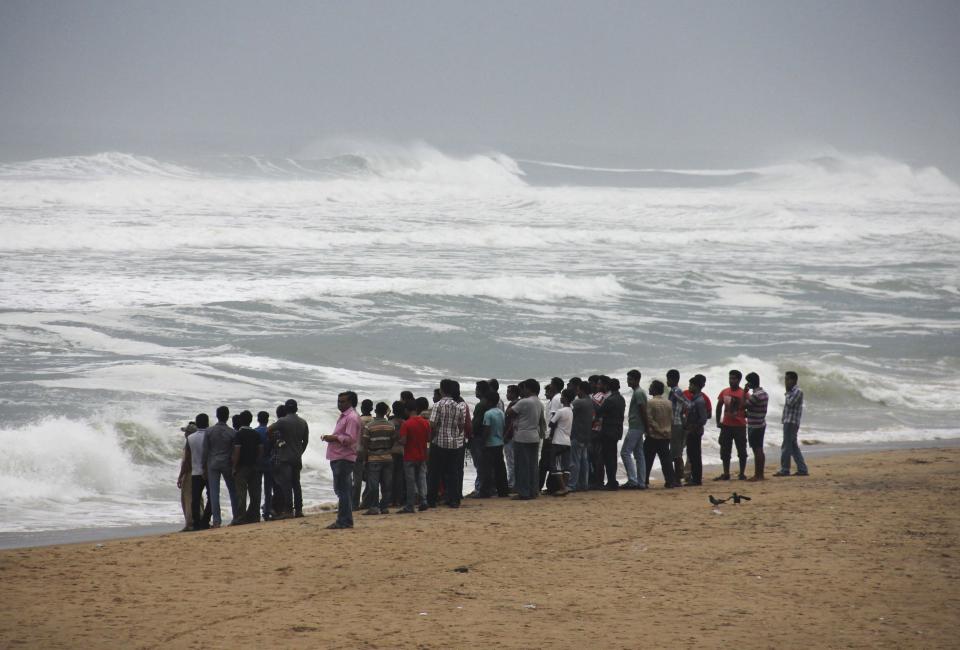 People watch as waves from the Bay of Bengal approach the shore at Podampata village