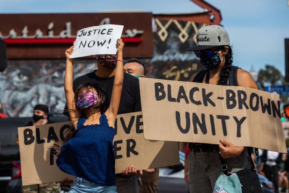 A girl jumps holding a sign while she and her family protest in the Boyle Heights neighborhood of Los Angeles on May 30. (Photo: APU GOMES via Getty Images)