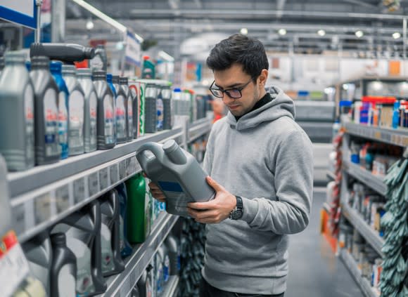 A man in a hoodie looking at engine oil in an auto parts store.