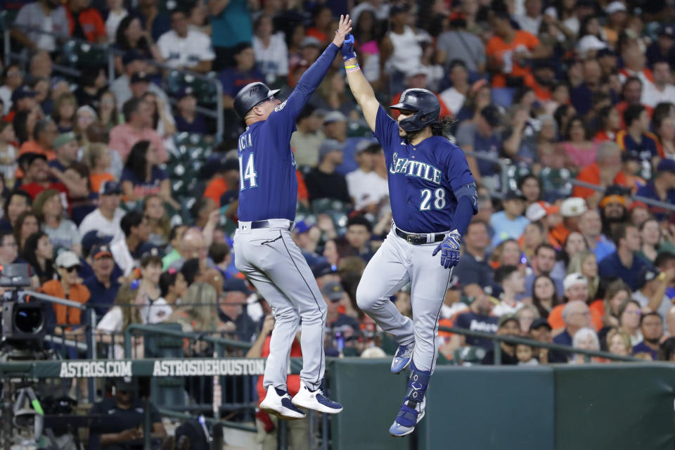 Seattle Mariners' Eugenio Suarez (28) celebrates with third base coach Manny Acta (14) while rounding the bases after hitting a two-run home run against the Houston Astros during the second inning of a baseball game Thursday, July 6, 2023, in Houston. (AP Photo/Michael Wyke).