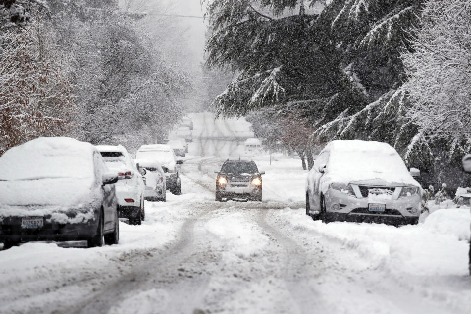 FILE - In this Feb. 11, 2019, file snow piles up on a street as a car maneuvers down the street in Seattle. With the eastern two-thirds of the U.S. shivering through an early blast of arctic air, it’s time to start thinking about whether your car’s tires will get you safely through the winter. (AP Photo/Elaine Thompson, File)