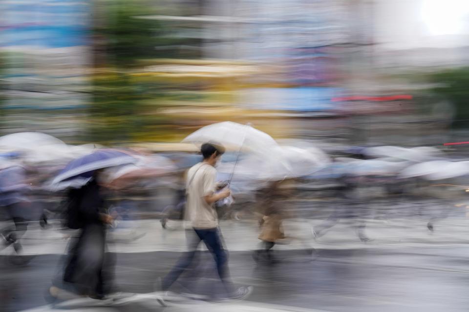 FILE - Morning commuters walk across an intersection in rain June 6, 2022, in Tokyo. As fossil fuel use that feeds climate change is creeping up around the world, Japan is set for another sweltering summer following last year’s dangerous heat waves and is at growing risk of flooding and landslides. (AP Photo/Kiichiro Sato, File)