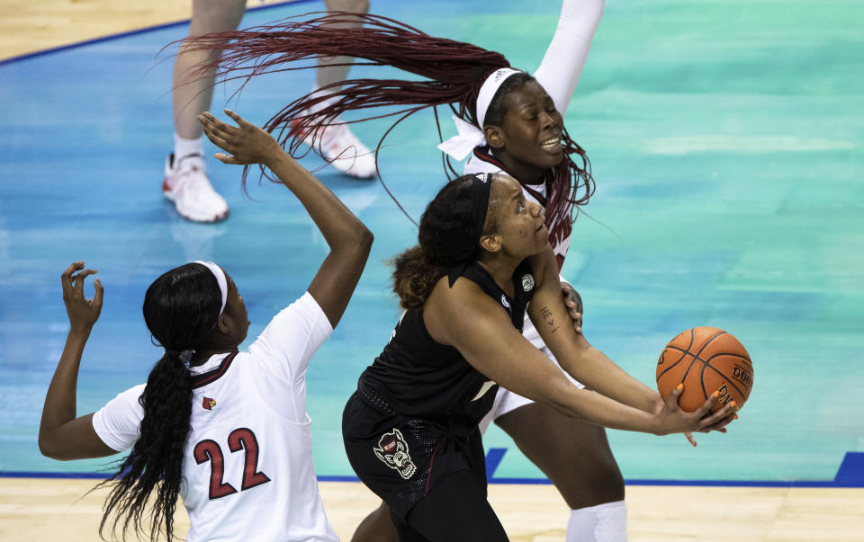 North Carolina State's Kayla Jones, center, attempts a shot ahead of Louisville's Olivia Cochran, right, and Elizabeth Dixon, left, during the championship of the Atlantic Coast Conference NCAA women's college basketball game in Greensboro, N.C., Sunday, March 7, 2021. (AP Photo/Ben McKeown)