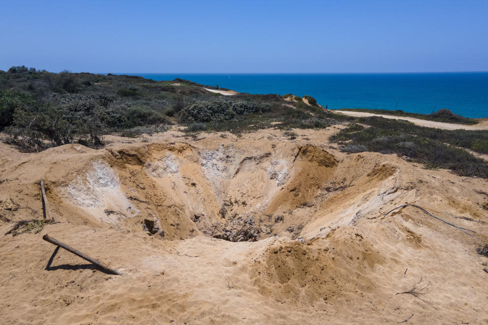 A massive crater sits in the sandy earth from explosions in the abandoned Israel Military Industries facility not far from Nissim Kahlon's home on the sandstone cliffs in Herzliya, Israel, Wednesday, June 28, 2023. Over half a century, Kahlon has transformed a tiny cave on a Mediterranean beach into an elaborate underground labyrinth filled with chiseled tunnels, detailed mosaic floors and a network of staircases and mysterious chambers. Fifty years after Kahlon moved into the home, Israel's Environmental Protection Agency has served him an eviction notice, claiming the structure threatens Israel's coastline. (AP Photo/Ariel Schalit)