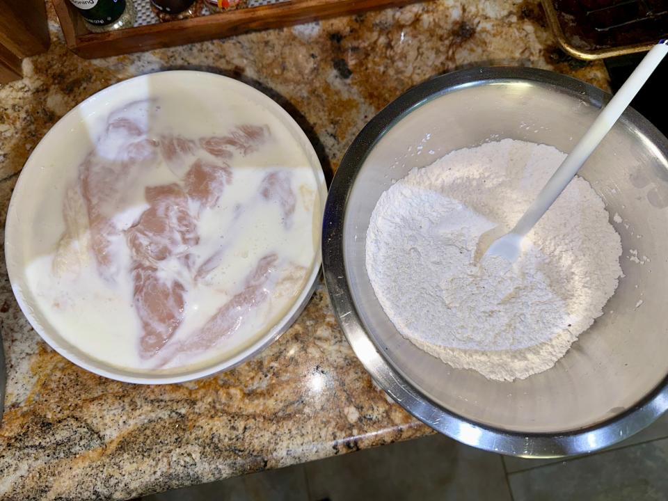 bowl of chicken in buttermilk and a bowl of flour on a kitchen counter