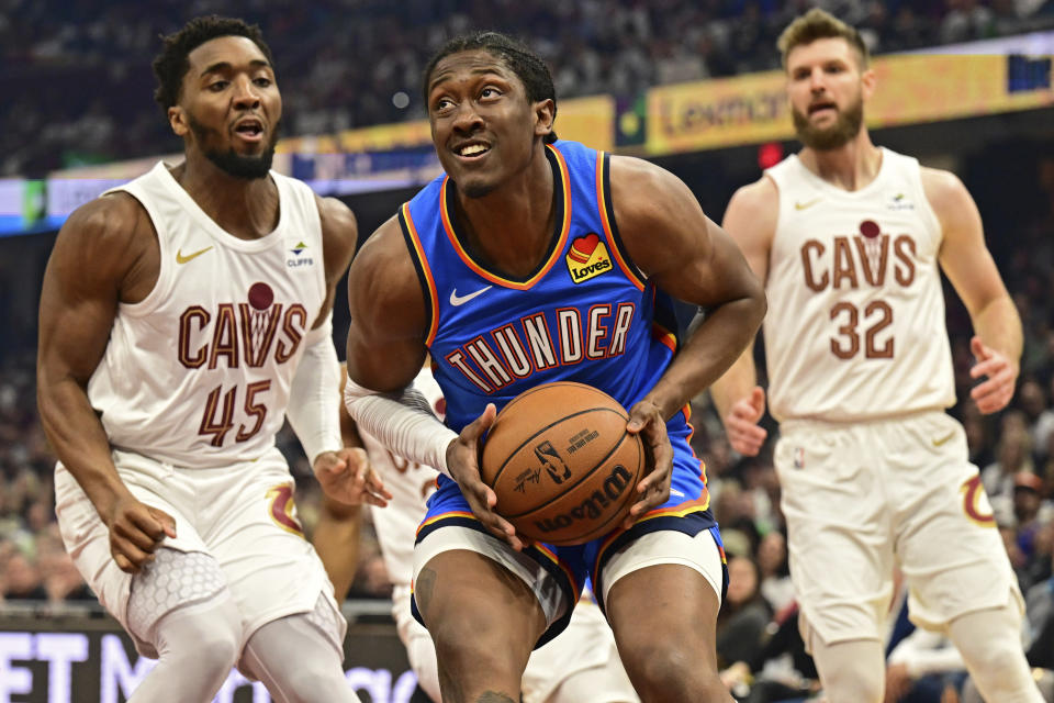 Oklahoma City Thunder forward Jalen Williams, center, goes to the basket against Cleveland Cavaliers guard Donovan Mitchell, left, and forward Dean Wade, right, in the first half of an NBA basketball game, Friday, Oct. 27, 2023, in Cleveland. (AP Photo/David Dermer)