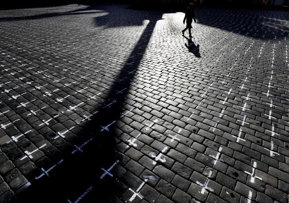 A woman walks by thousands of crosses that are painted at the Old Town Square, to commemorate the 1-year anniversary of the death of first Czech COVID-19 patient, in Prague, Czech Republic, Monday, March 22, 2021. Some 25,000 have been killed by COVID-19 in the hard-hit Czech Republic. Jaromir Vytopil was one of them. His everyday presence in the small Czech town of Pelhrimov was something everybody took for granted for seven decades as he had served the generations of readers. The longest serving Czech bookseller, passed away on Nov 9. 2020, at age of 83. (AP Photo/Petr David Josek)