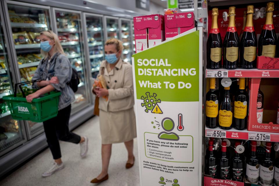 Shoppers wearing PPE (personal protective equipment), of a face mask or covering as a precautionary measure against spreading COVID-19,, walk past a banner advising customers to maintain the British government's current social distancing guidelines and stay two metres (2M) apart, inside an Asda supermarket store in Walthamstow, east London on June 22, 2020. - Britain's current social distancing guidelines set the distance between each person at two metres to avoid the risk of contamination to coronavirus. There is pressure on the government to reduce this distance in order to give a boost to bars, restaurants and hotels, which are scheduled to reopen next month. (Photo by Tolga AKMEN / AFP) (Photo by TOLGA AKMEN/AFP via Getty Images)