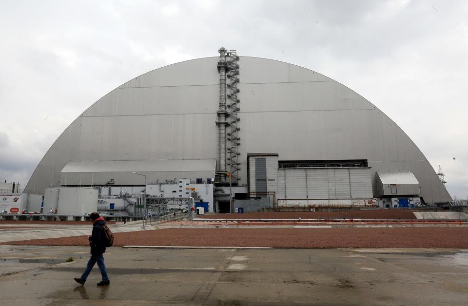 A man walks past a shelter covering the exploded reactor at the Chernobyl nuclear plant, in Chernobyl, Ukraine, Thursday, April 15, 2021.