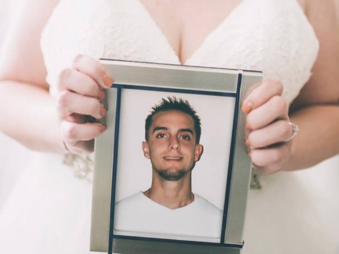 Trish Penny holding a framed picture of her brother, Luke, who died in a workplace accident on May.19, 2010, when he was working in a trench in Whitby, Ont., and a concrete wall caved in, collapsing on top of him.  (Submitted by Trish Penny - image credit)