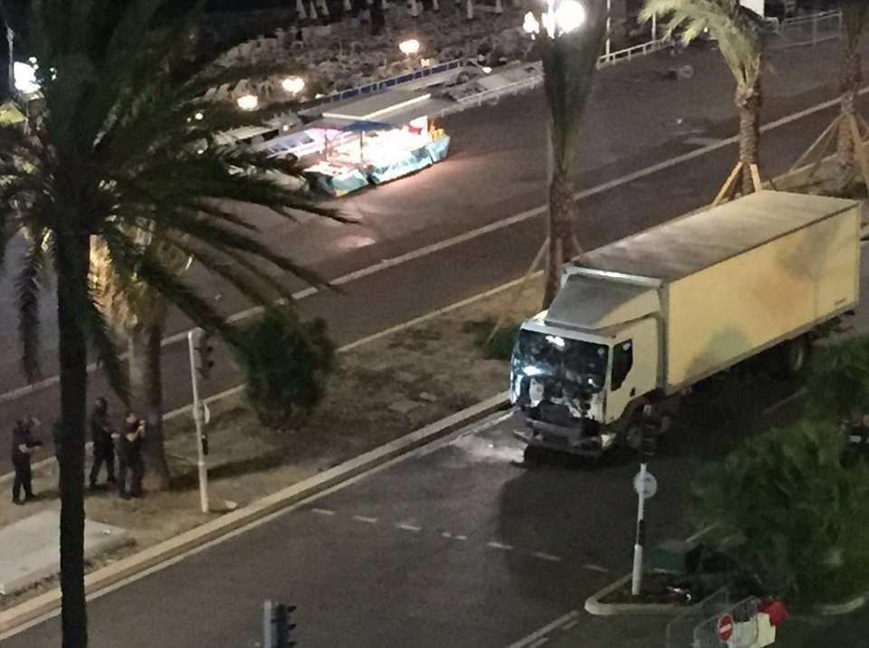 Police officers keep their distance and using palm trees as cover while approaching a bullet-ridden lorry.