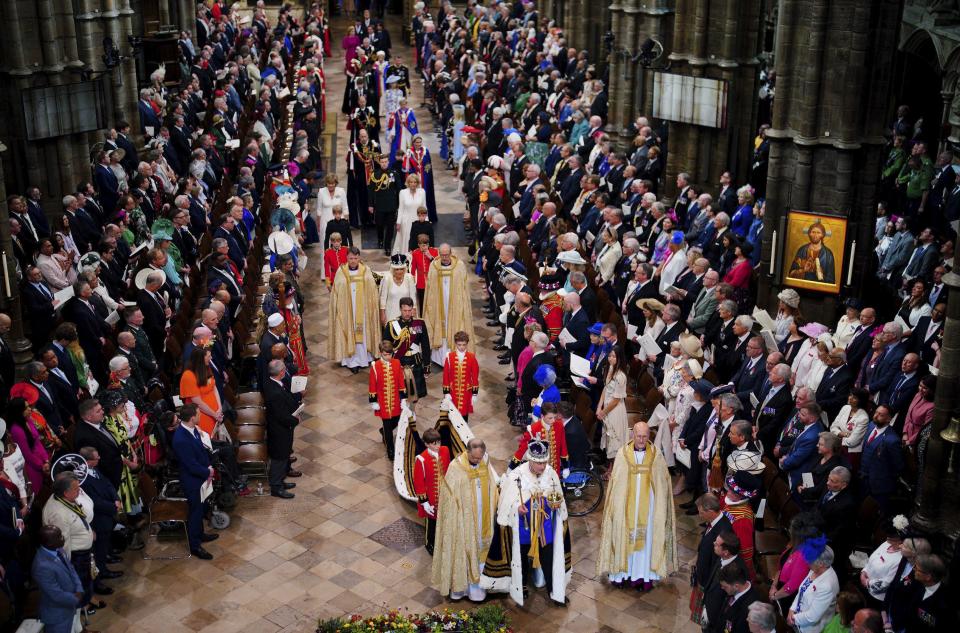 King Charles III, wearing the Imperial State Crown, followed by Queen Camilla, leaves Westminster Abbey in central London following his coronation ceremony.