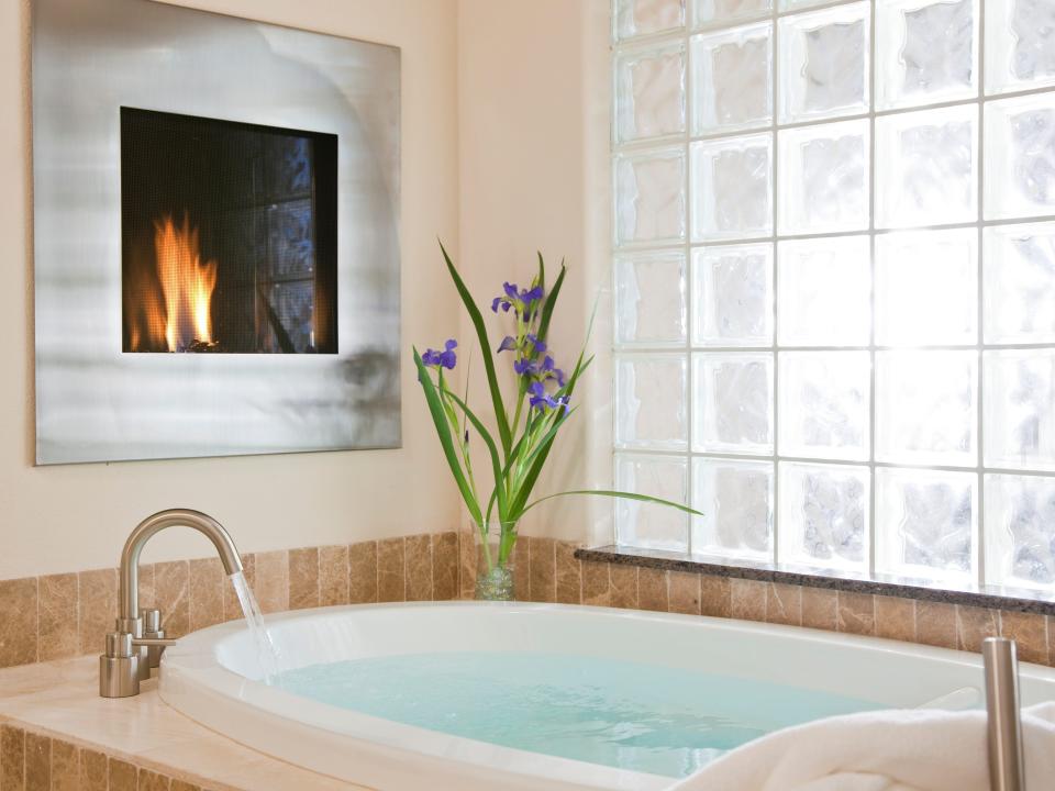 A sleek, modern bathtub filled with water facing a fireplace