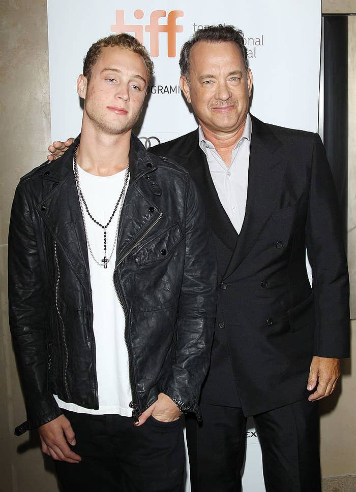 Chet Hanks, wearing a leather jacket and t-shirt, stands next to Tom Hanks in a dark suit at the Toronto International Film Festival