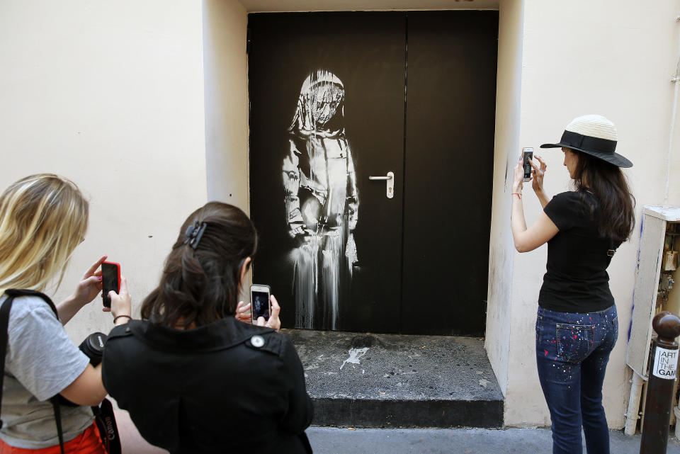 People take pictures of an artwork attributed to street artist Banksy on June 26, 2018 in Paris, France, on a side street by the Bataclan concert hall where a terrorist attack killed 90 people on November 13, 2015. / Credit: Chesnot / Getty Images