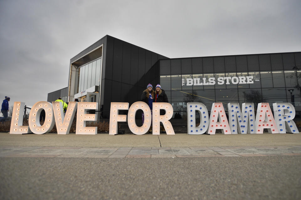 Fans stand for photographs by a sign in support of Buffalo Bills safety Damar Hamlin outside Highmark Stadium before an NFL football game against the New England Patriots, Sunday, Jan. 8, 2023, in Orchard Park, N.Y. Hamlin remains hospitalized after suffering a catastrophic on-field collapse in the team's previous game against the Cincinnati Bengals. (AP Photo/Adrian Kraus)