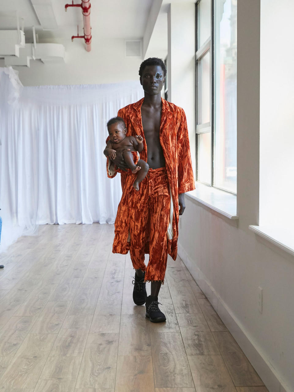 <p>Model wears an orange crushed velvet robe and trousers while carrying a baby at the Collina Strada Fall/Winter 2018 show. (Photo: Jonathan Hokklo) </p>