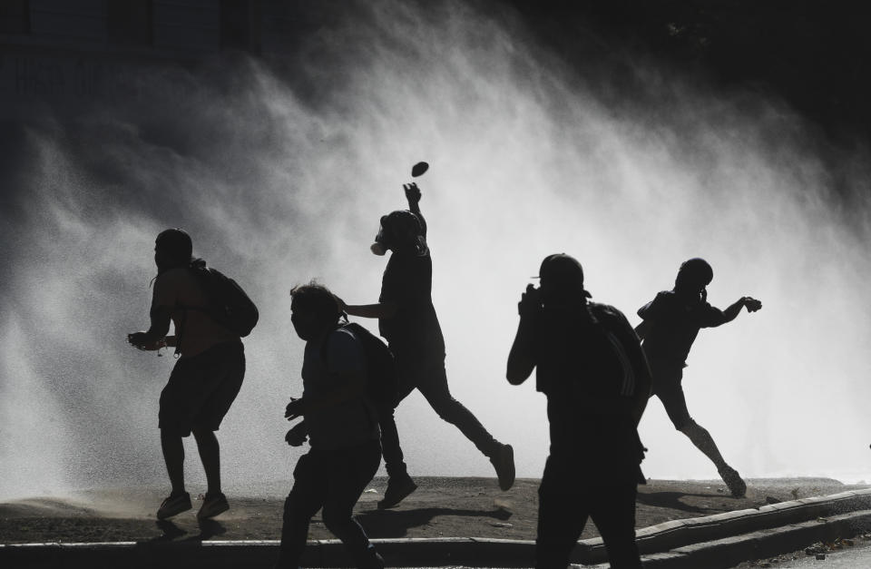 Anti-government demonstrators throw rocks at a police water cannon trying to disperse them in Santiago, Chile, Friday, Dec. 27, 2019. Chile has been roiled by continuing and sometimes violent street protests since Oct. 18, when a student protest over a modest increase in subway fares turned into a much larger and broader movement with a long list of demands that largely focus on inequality. (AP Photo/Fernando Llano)