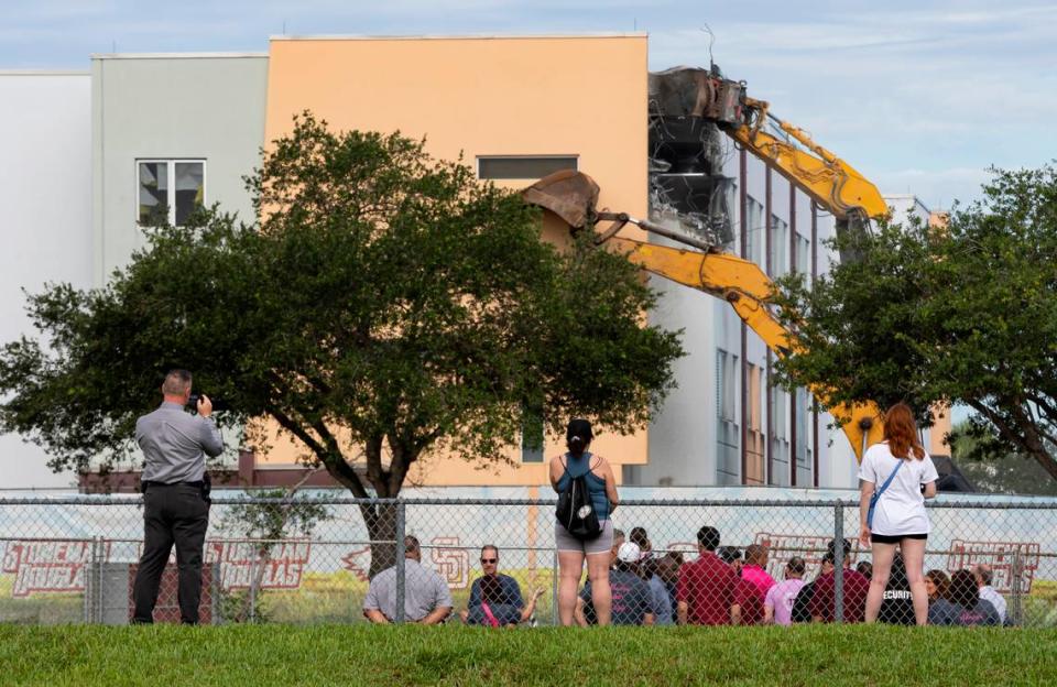 People watch as crews use heavy equipment to tear down the 1200 building of Marjory Stoneman Douglas High School on Friday, June 14, 2024, in Parkland, Fla. On February 14, 2018, a gunmen entered the school and killed 17 people.