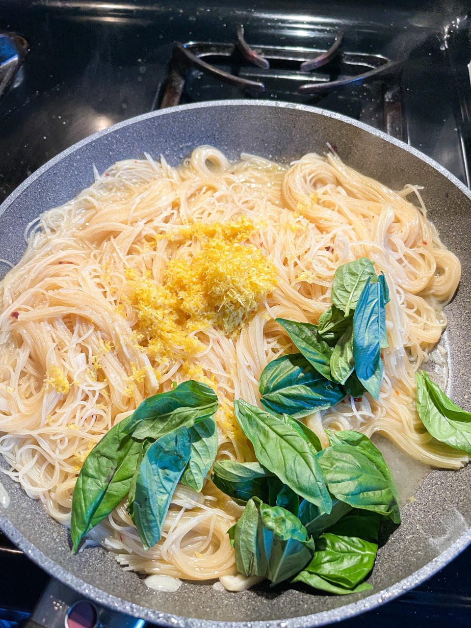 Lemon zest and basil leaves added to pasta in pan
