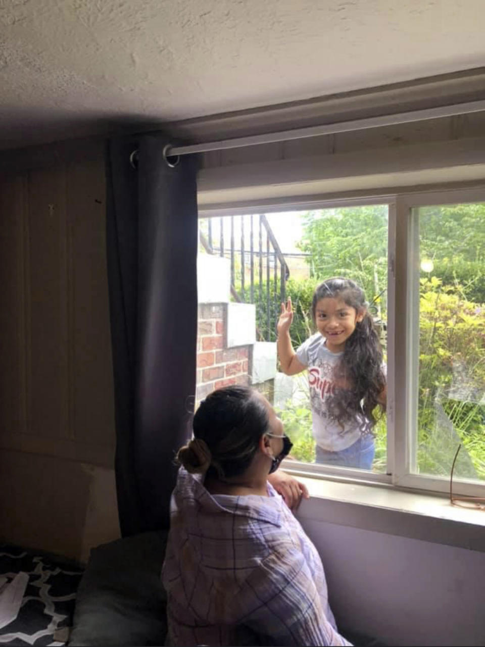 Allison, 5, plays peek-a-boo with her mother Janeth from outside her bedroom window in this family photograph after both of her parents were both diagnosed with COVID-19, Thursday May 7, 2020, at their home in Washington. (Janeth via AP)