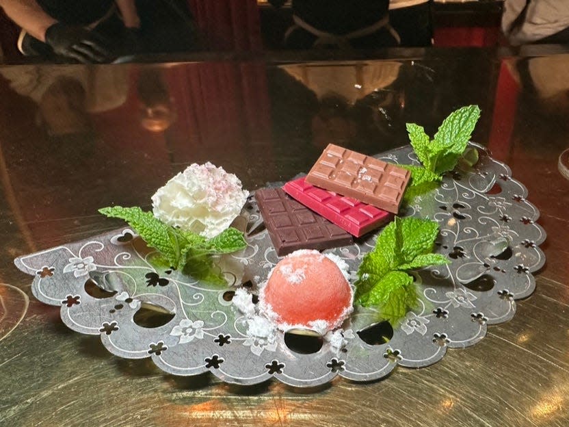 black half-circle with scalloped edges topped with small bars of chocolate, leaves, and other items