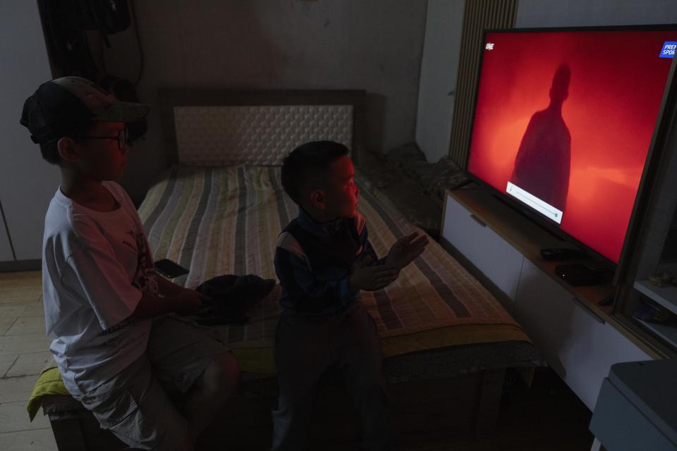 Twelve-year-old Gerelt-Od Kherlen, left, watches a sports channel with his younger brother Gerelt-Ireedui Kherlen at their home in a Ger district on the outskirts of Ulaanbaatar, Mongolia, Tuesday, July 2, 2024. Growing up in a Ger district without proper running water, Gerelt-Od fetched water from a nearby kiosk every day for his family. Carrying water and playing ball with his siblings and other children made him strong and resilient. (AP Photo/Ng Han Guan)