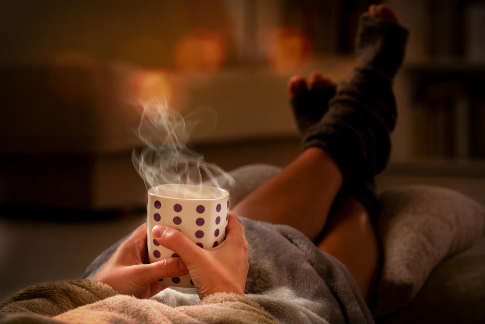 Woman with cup of hot drink  and feet lying on pilow in the cozy room