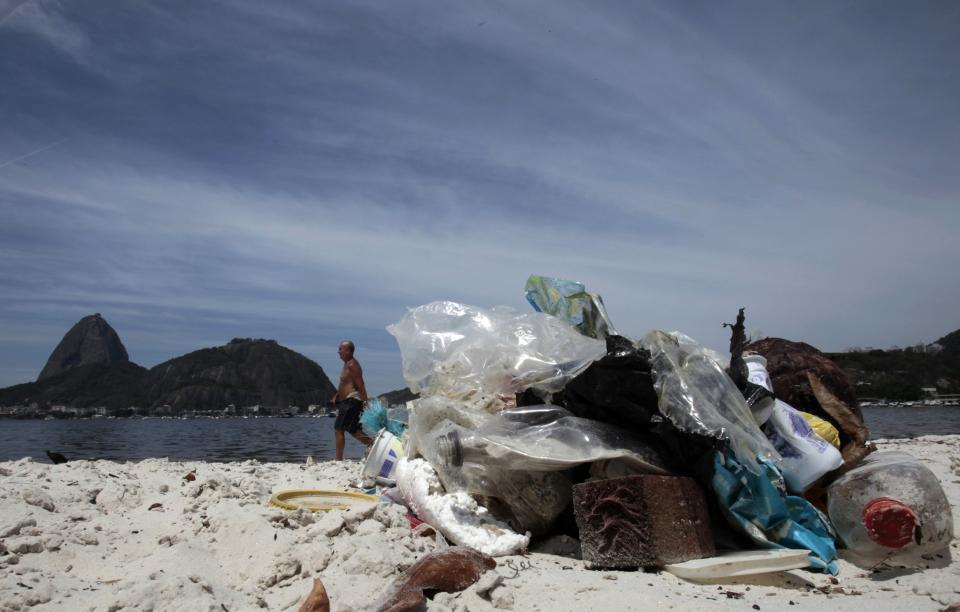 A man walks, with the Sugar Loaf Mountain in the background, near garbage on Botafogo beach in the Guanabara Bay in Rio de Janeiro March 12, 2014. According to the local media, the city of Rio de Janeiro continues to face criticism locally and abroad that the bodies of water it plans to use for competition in the 2016 Olympic Games are too polluted to host events. Untreated sewage and trash frequently find their way into the Atlantic waters of Copacabana Beach and Guanabara Bay - both future sites to events such as marathon swimming, sailing and triathlon events. Picture taken on March 12, 2014. REUTERS/Sergio Moraes (BRAZIL - Tags: ENVIRONMENT SPORT OLYMPICS)