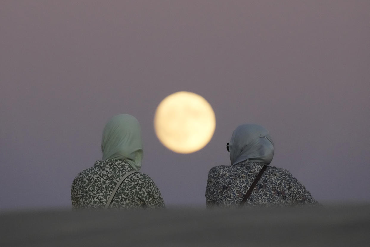 An image of two women from behind with the outline of the supermoon between them.