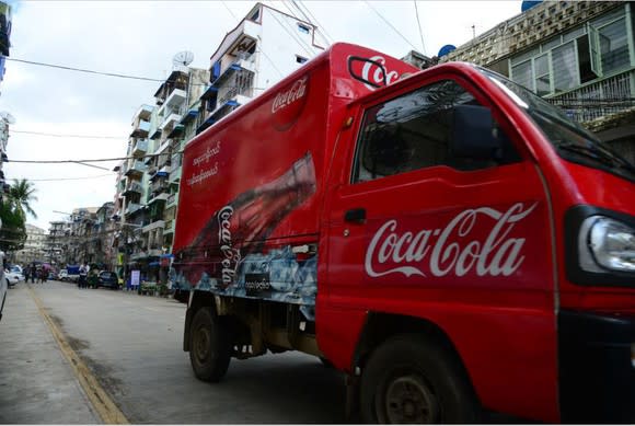 A Coca-Cola truck parked on the street out in front of businesses.