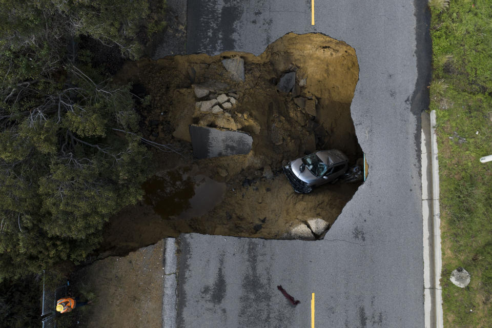 In this image taken with a drone, a vehicle is stuck in a sinkhole in the Chatsworth section of Los Angeles, Tuesday, Jan. 10, 2023. Sinkholes swallowed cars and raging torrents swamped towns and swept away a small boy Tuesday as California was wracked by more wild winter while the next system in a powerful string of storms loomed on the horizon. (AP Photo/Jae C. Hong)