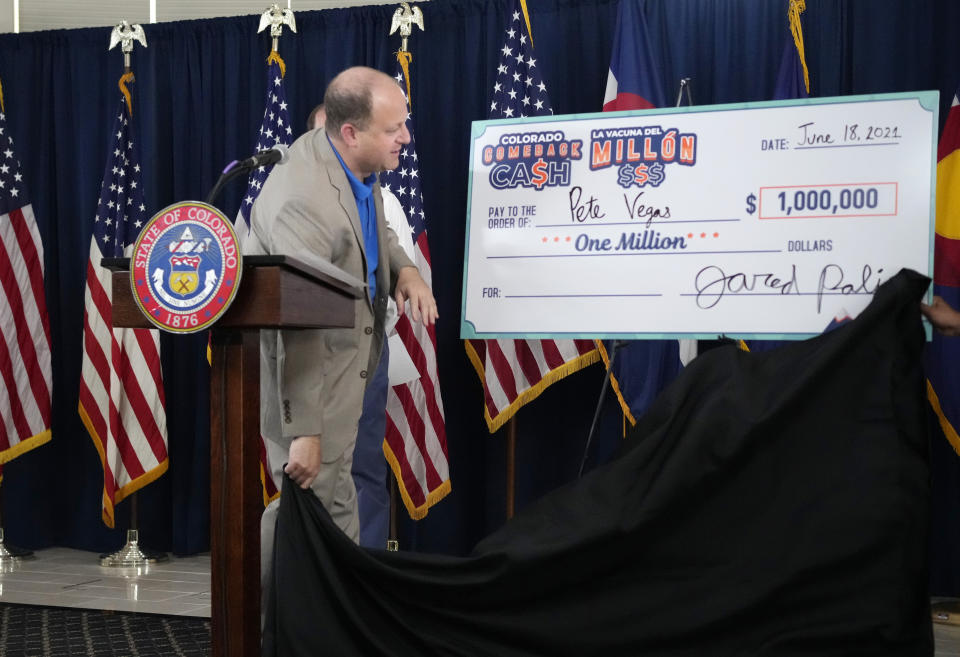 Colorado Governor Jared Polis pulls the wraps off a check for Peter Vegas of Boulder, Colo., who was announced as the third of five weekly $1-million winners for being vaccinated against COVID-19 during a news conference Friday, June 18, 2021, in Denver. (AP Photo/David Zalubowski)