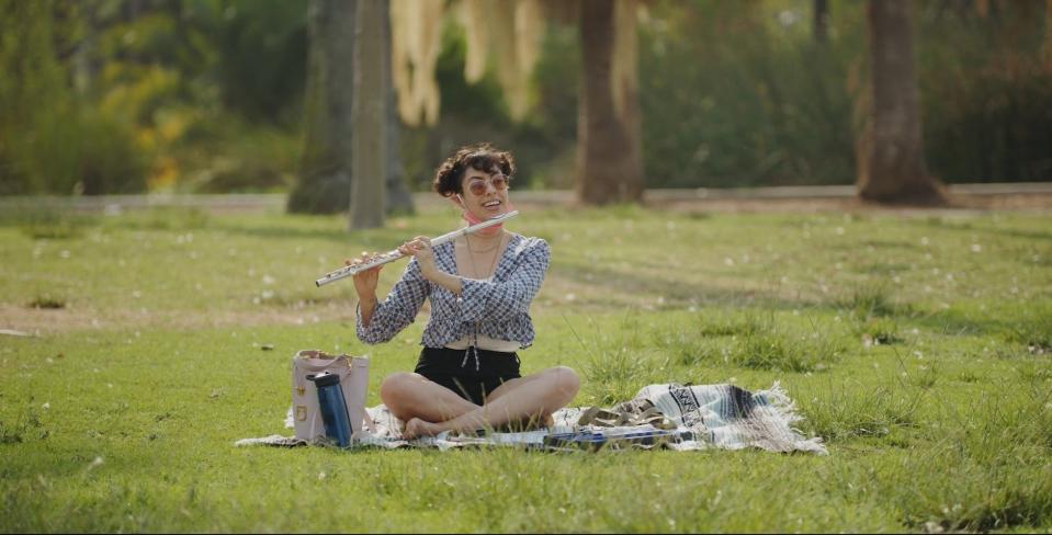 A person in a park seated on blanket playing the flute