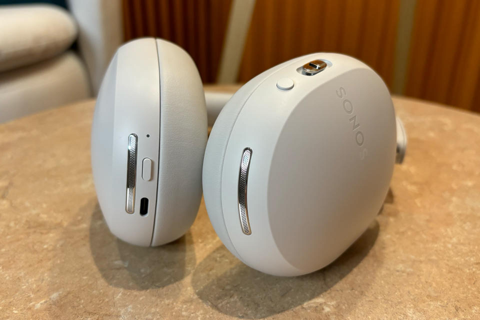White headphones laying flat on a small table, showing the buttons on both sides. 
