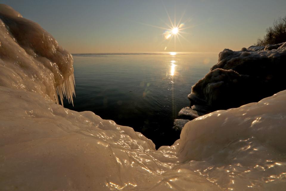 The sun rises above ice formations off the shore of Lake Michigan at Big Bay Park in Whitefish Bay Saturday, Feb. 20, 2021. Due to below-zero temperatures, much of the shoreline is frozen over leaving tree branches covered in ice.