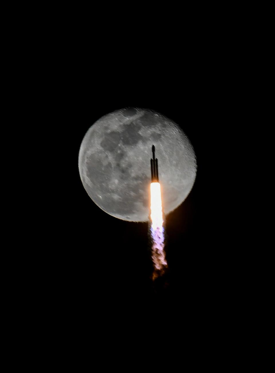 A SpaceX Falcon Heavy rocket flies across the face of the moon after liftoff from Kennedy Space Center on Thursday, December 28, 2023.